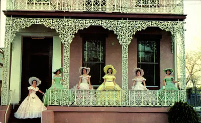 Mulheres em vestidos de estilo vitoriano — diante de uma casa com portico decorado — editor Express Publishing Co., Inc., Baton Rouge, USA