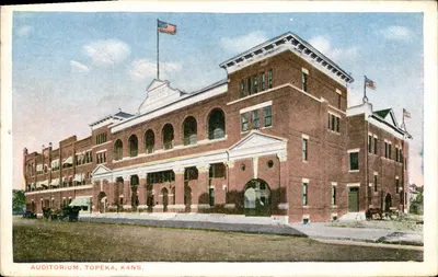 Auditório, Topeka, Kansas — edifício de tijolos com arcadas e bandeiras americanas — editor não identificado