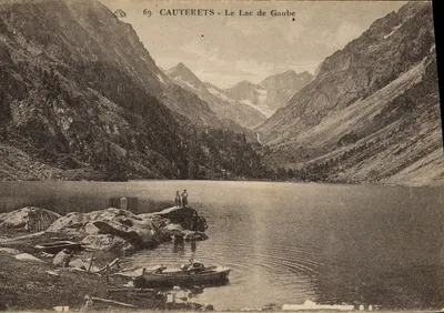 Cauterets - Le Lac de Gaube — vue du lac entouré de montagnes, avec deux personnes sur un rocher et une barque à l'avant-plan — n° 69
