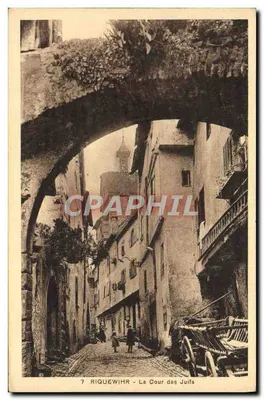 Riquewihr - La Cour des Juifs — view under a stone arch with buildings and handcart